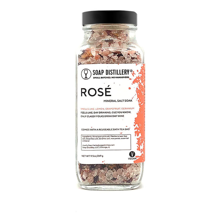 An image of a tall glass jar with a black lid. Through the jar, you can see a mix of pink and white salts.The label says Soap Distillery, Rosé Mineral Salt Soak.