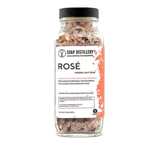 An image of a tall glass jar with a black lid. Through the jar, you can see a mix of pink and white salts.The label says Soap Distillery, Rosé Mineral Salt Soak.