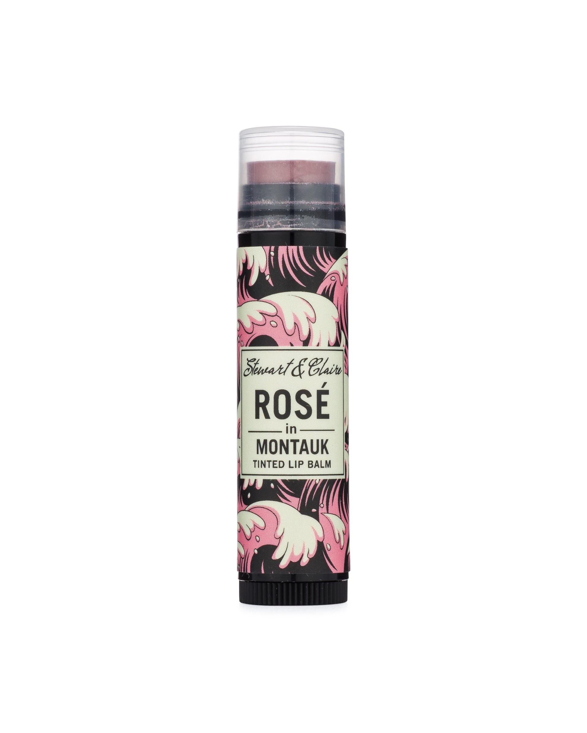An image of a .15 ounce black plastic tube with a clear cap. Through the cap, you can see a lip balm that is a dusky pink. The tube has a label in pink, black, and white with a wave pattern. In the center of the balm is an off-white square that says Stewart & Claire in black script and then Rosé in Montauk, Tinted Lip Balm underneath.