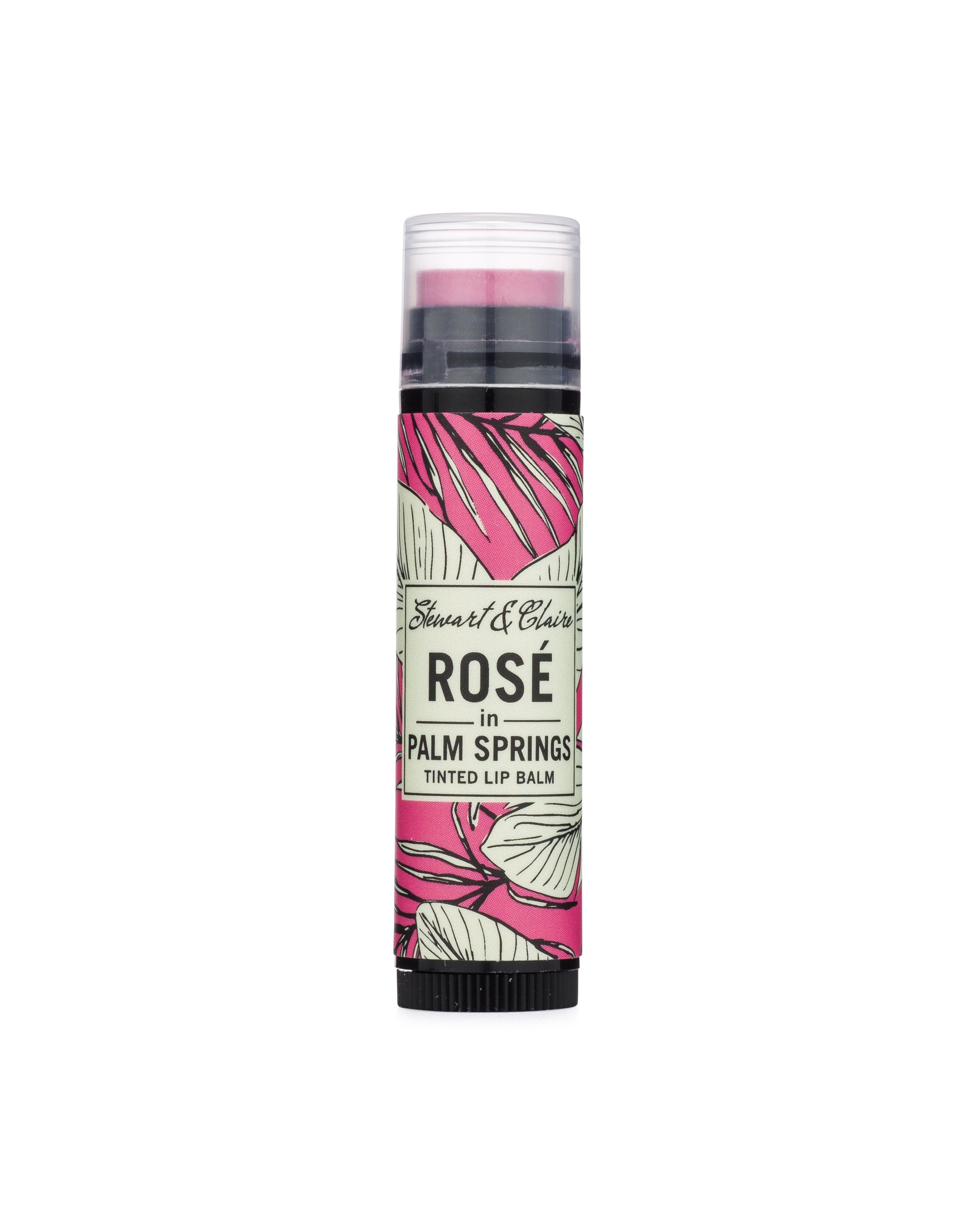 An image of a .15 ounce black plastic tube with a clear cap. Through the cap, you can see a lip balm that is a bright pink. The tube has a label in pink, black, and white with a leafy pattern. In the center of the balm is an off-white square that says Stewart & Claire in black script and then Rosé in Palm Springs, Tinted Lip Balm underneath.