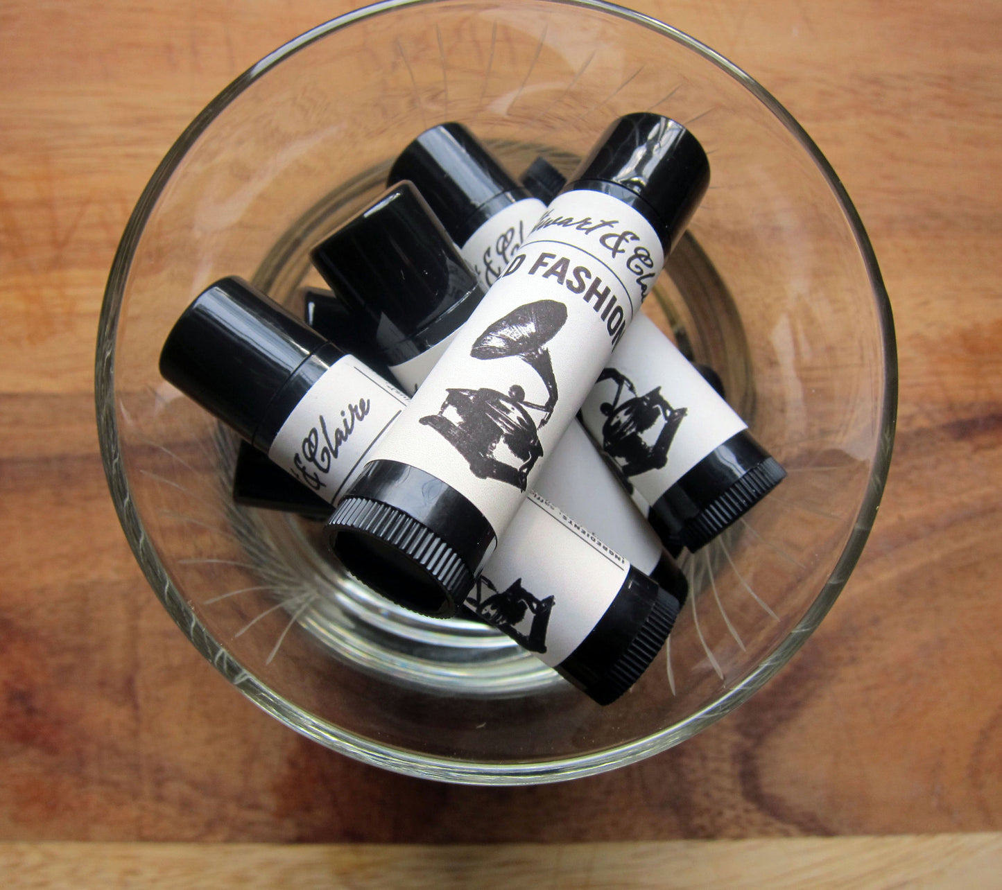 An image of a glass filled with .15 ounce black plastic tubes with an off-white label. The top of the label says Stewart & Claire in black script. Underneath says Old Fashioned. There is a black and white illustration of a gramophone.