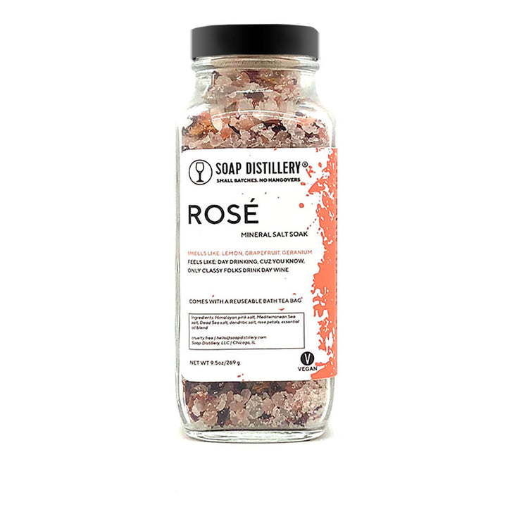 An image of a tall glass jar with a black lid. Through the jar, you can see a mix of pink and white salts.The label says Soap Distillery, Rosé Mineral Salt Soak. 