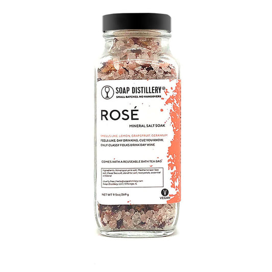 An image of a tall glass jar with a black lid. Through the jar, you can see a mix of pink and white salts.The label says Soap Distillery, Rosé Mineral Salt Soak. 