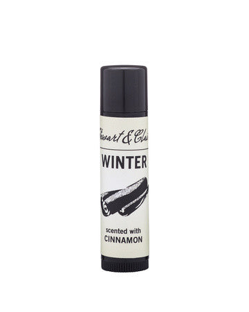 An image of a black plastic lip balm tube with an off-white label. The label says STeart & Claire in black script at the top. Underneath, it says Winter. Underneath that is a black and white illustraiton of cinnamon sticks and it says scented with cinnamon. 